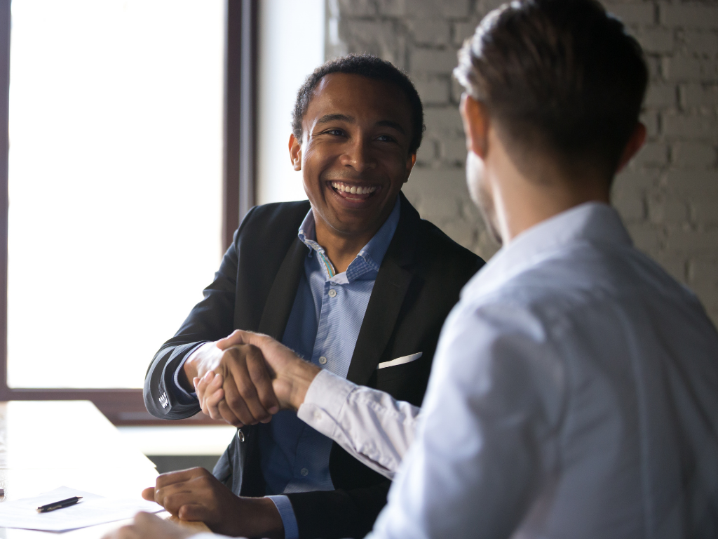 2 men shaking hands at a table on is smiling in the direction of the camera.