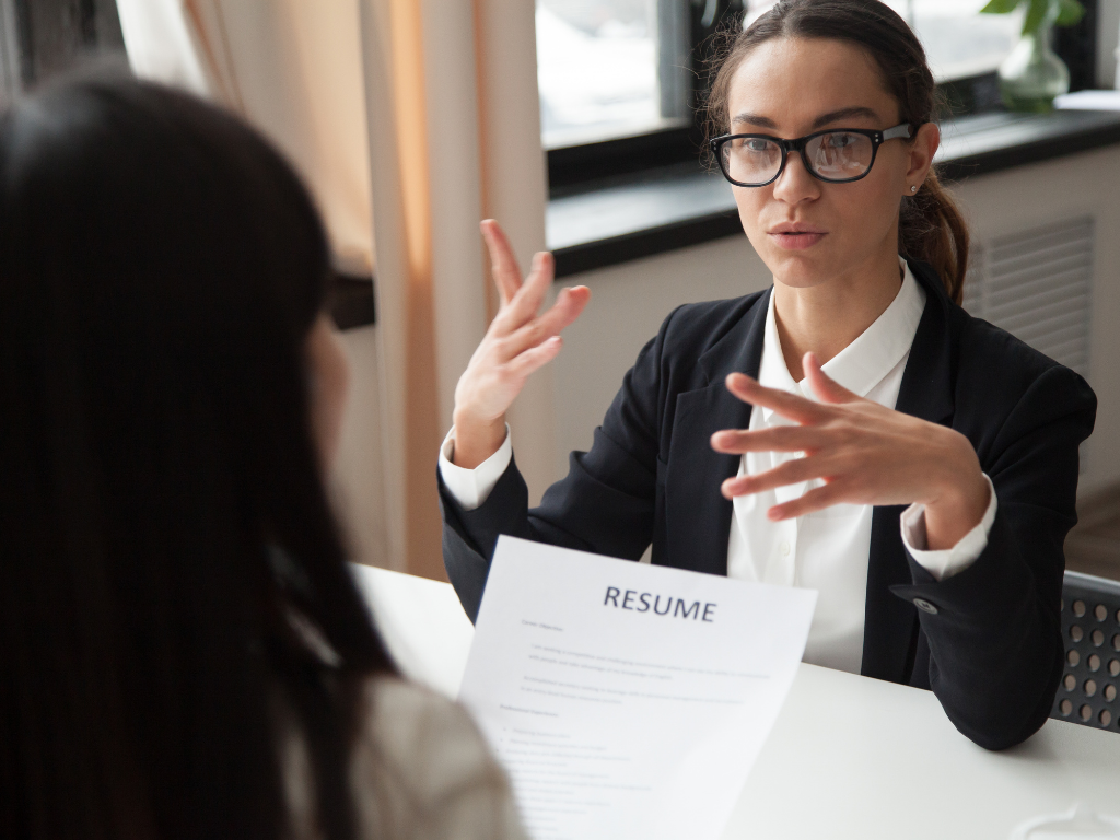 2 women in law firm interview setting in business attire; one woman looking at resume other woman talking.