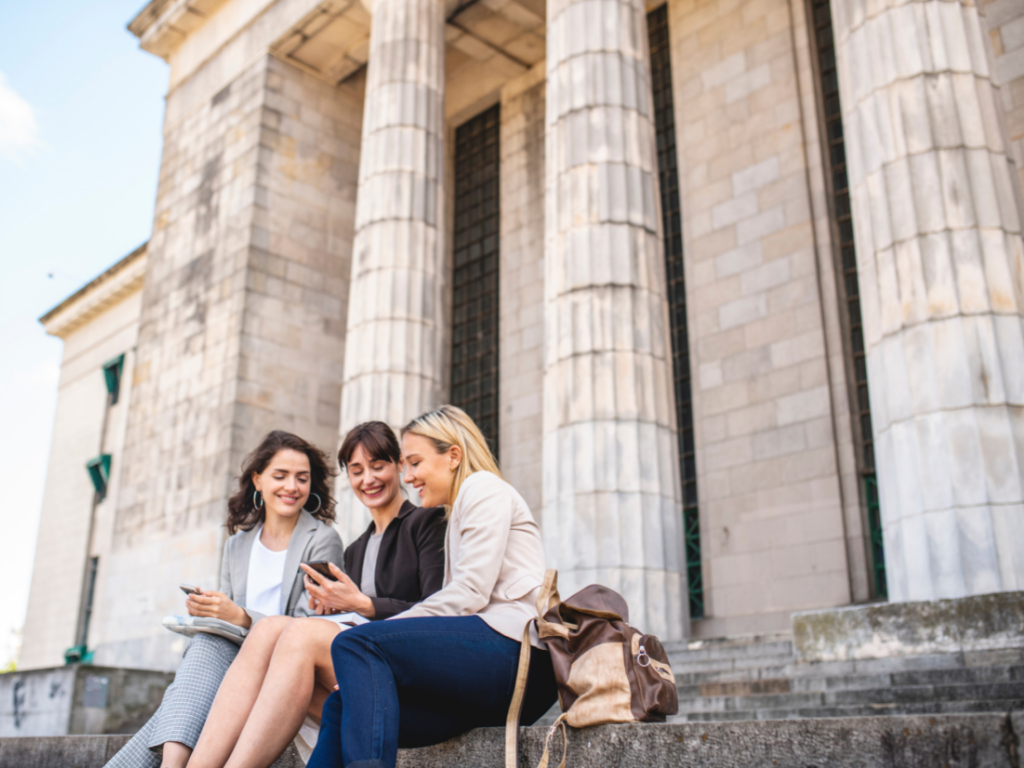 3 women looking at phones on steps of government building; going to law school