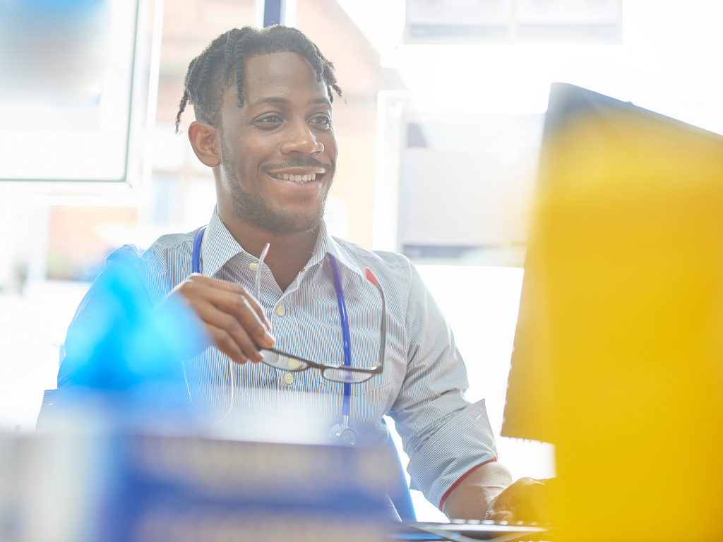 Man looking at computer with glasses in hand smiling