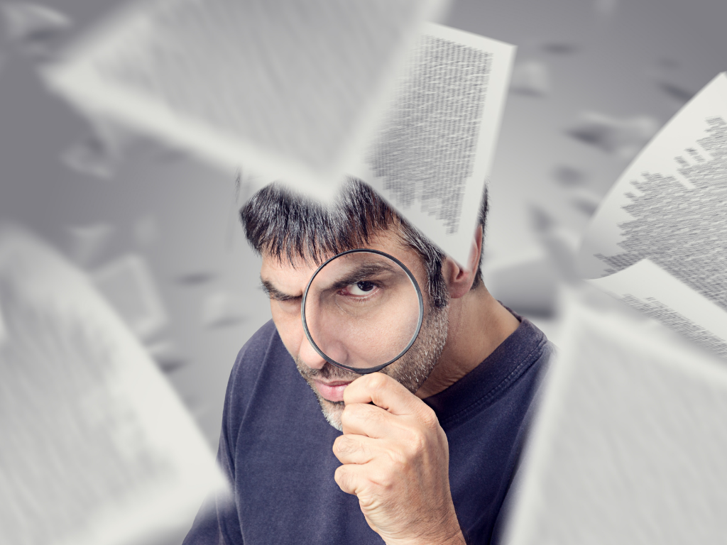 Man in blue shirt looking through magnifying glass with paper flying around in the sky