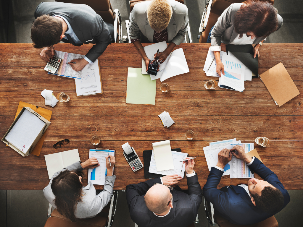 Team of six people all dressed up in suits working a table discussing papers in front of them