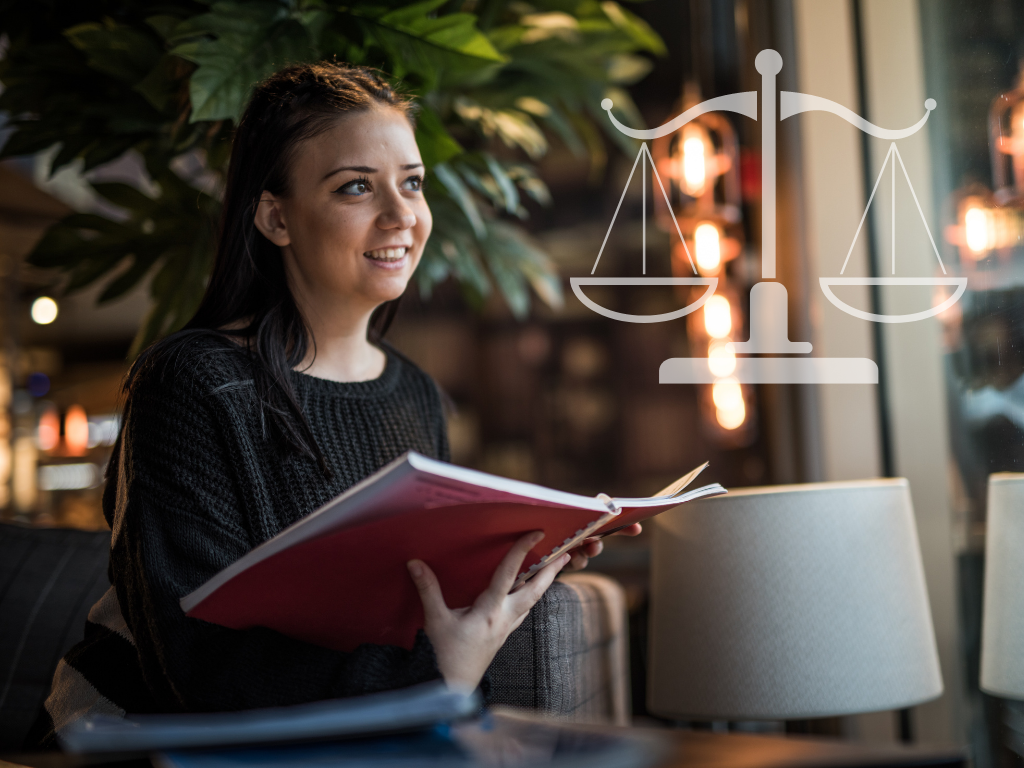 Woman in a sweater sitting in a library looking at book and staring at the scales of justice