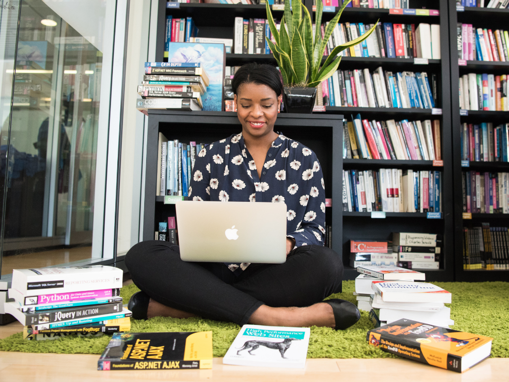 Woman sitting on the floow with laptop in lap and books surrounding her.