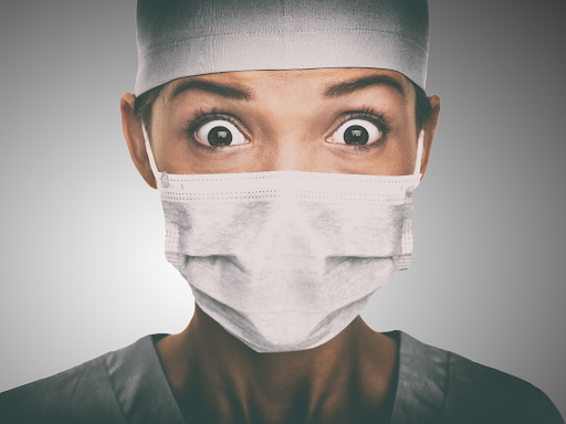 A nurse looking perplexed with wide eyes in face mask, cap and scrubs