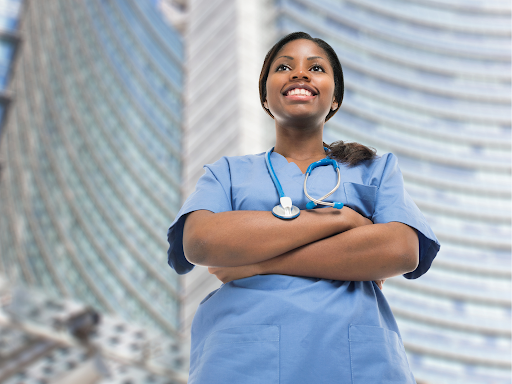 A nurse standing in front of a large building with blue scrubs and a stethescope