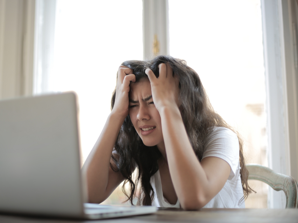 Woman looking at computer with hands on her head.