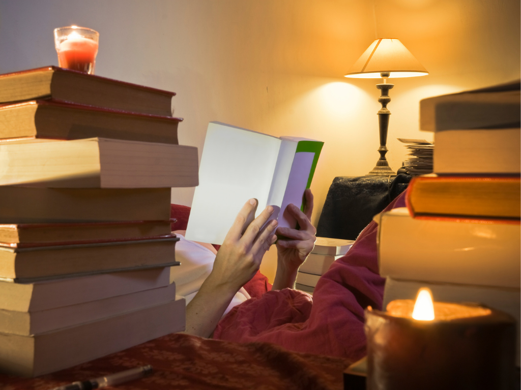 Hands holding book in candle and lamplight surrounded by other books