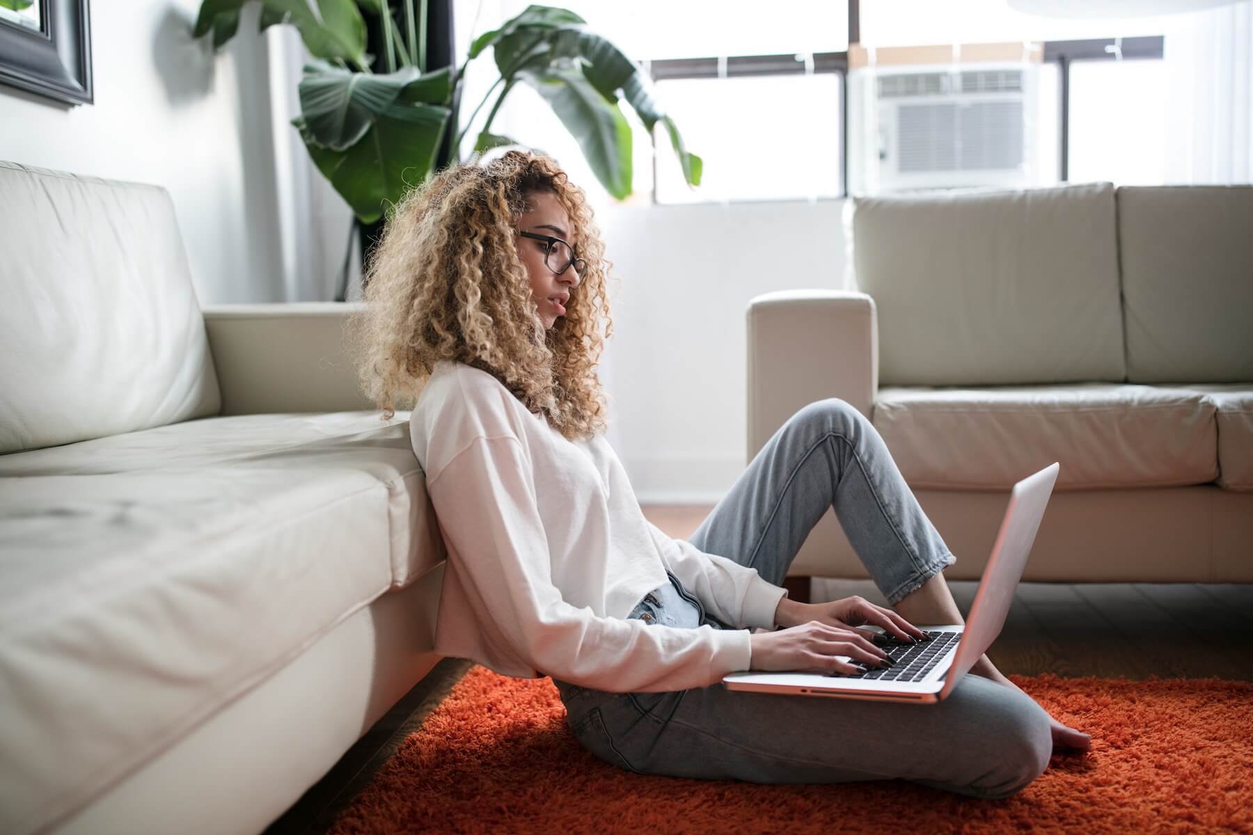 Woman sitting on the living room floor, studying flashcards on a laptop computer.