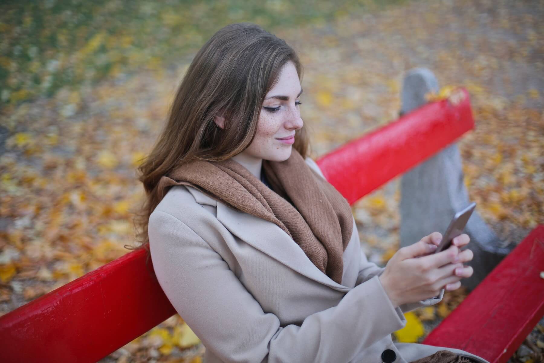 Woman sitting on a park bench, focused on studying on her smartphone.