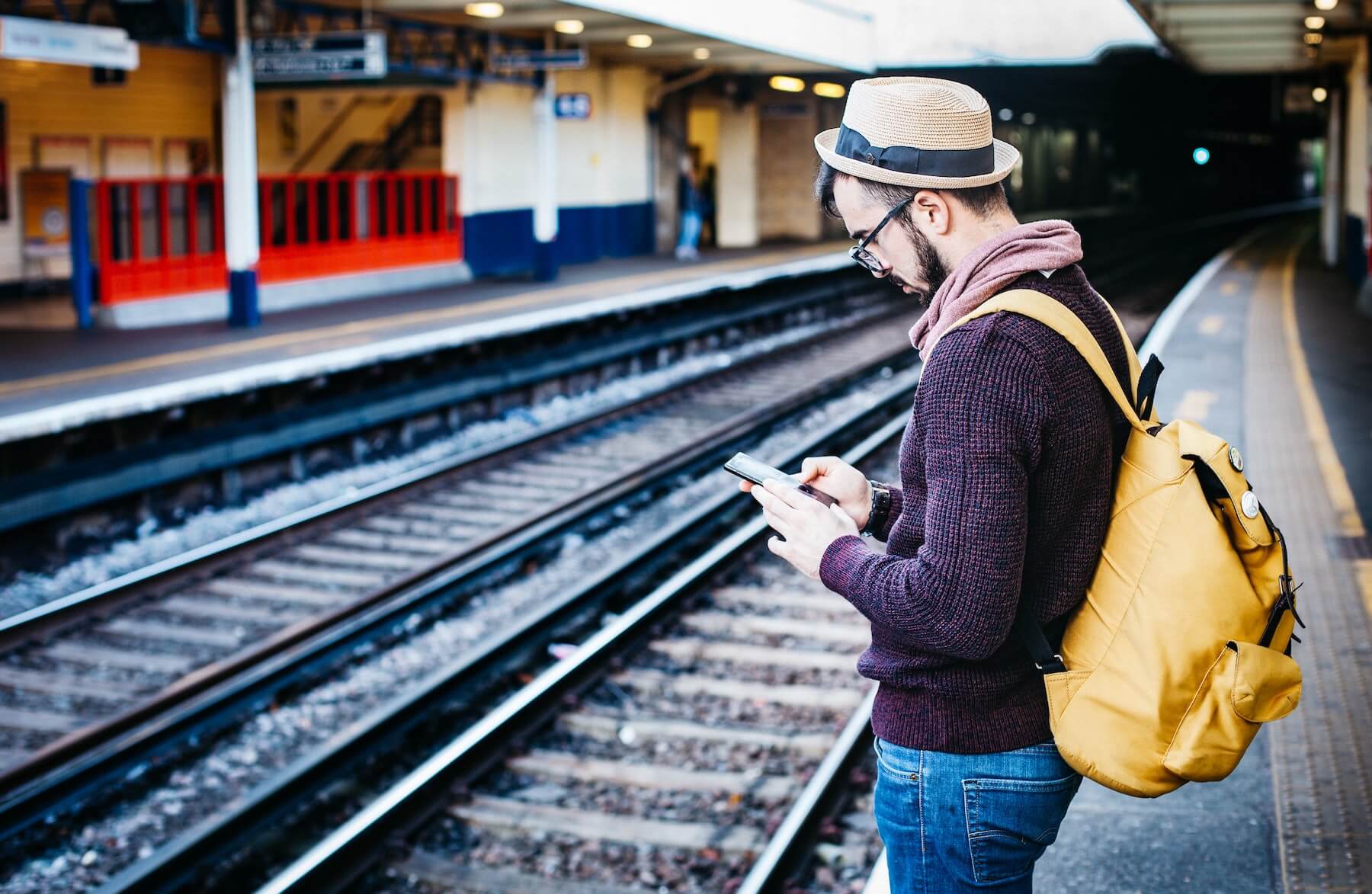Man standing near train tracks, focused on studying on his mobile phone.